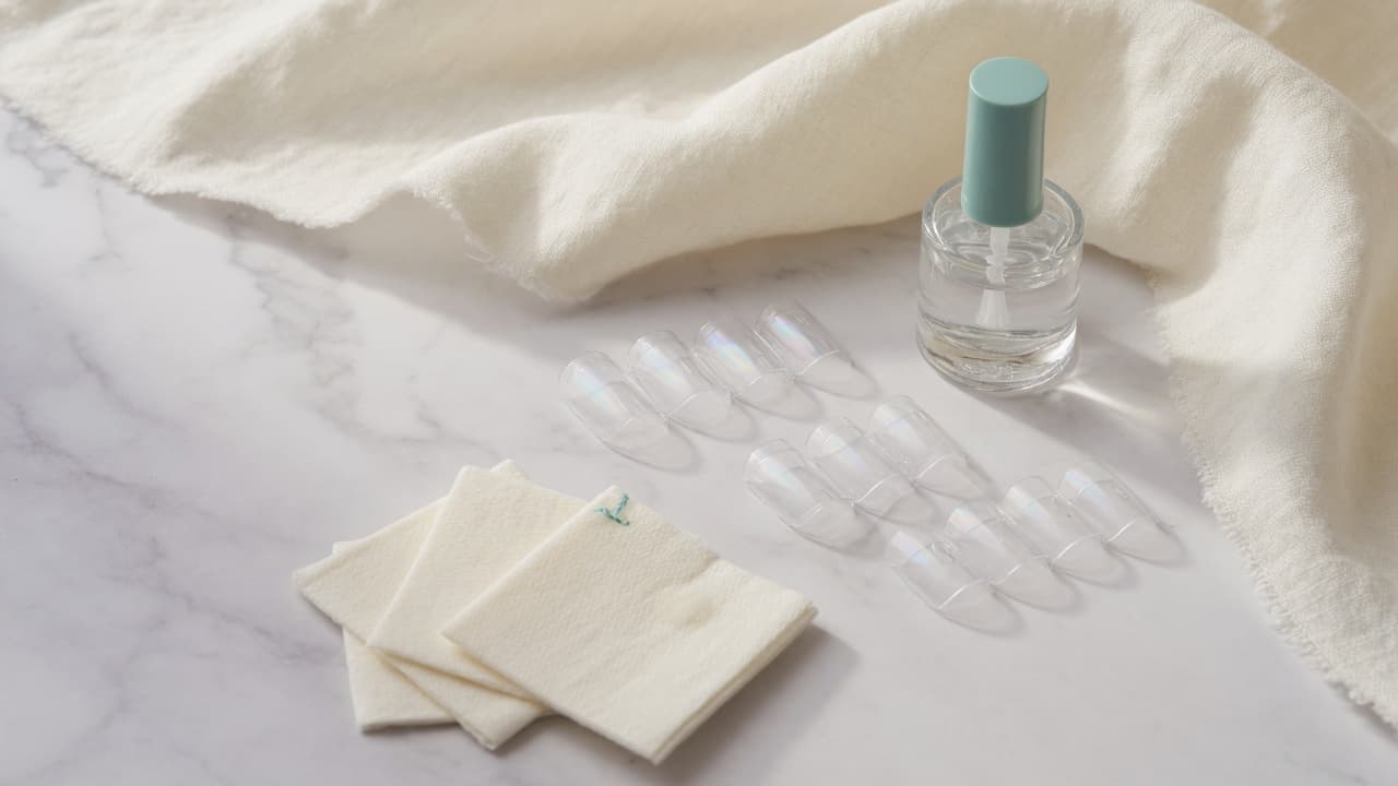 Clear nail covers, adhesive bottle, and prep wipes arranged on white marble