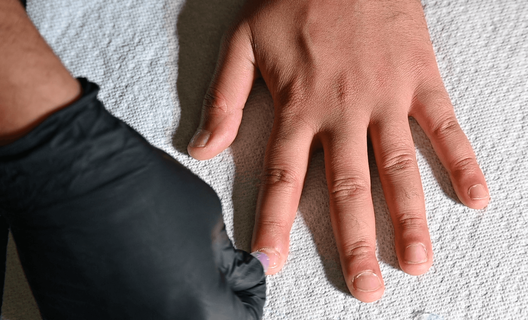 Gloved hand placing a clear protective nail cover onto the fingernail
